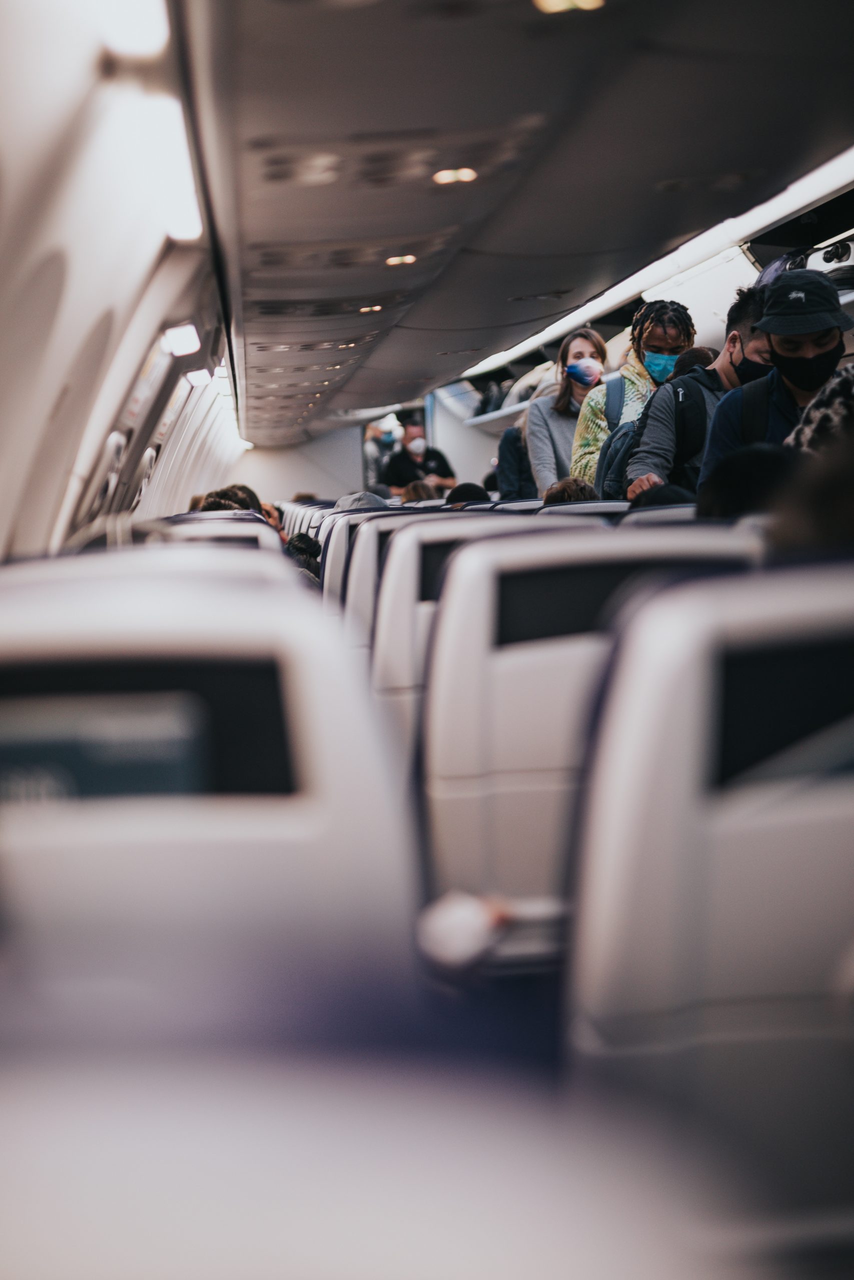 This image shows passengers boarding an airplane and lined up in the aisle while wearing masks.