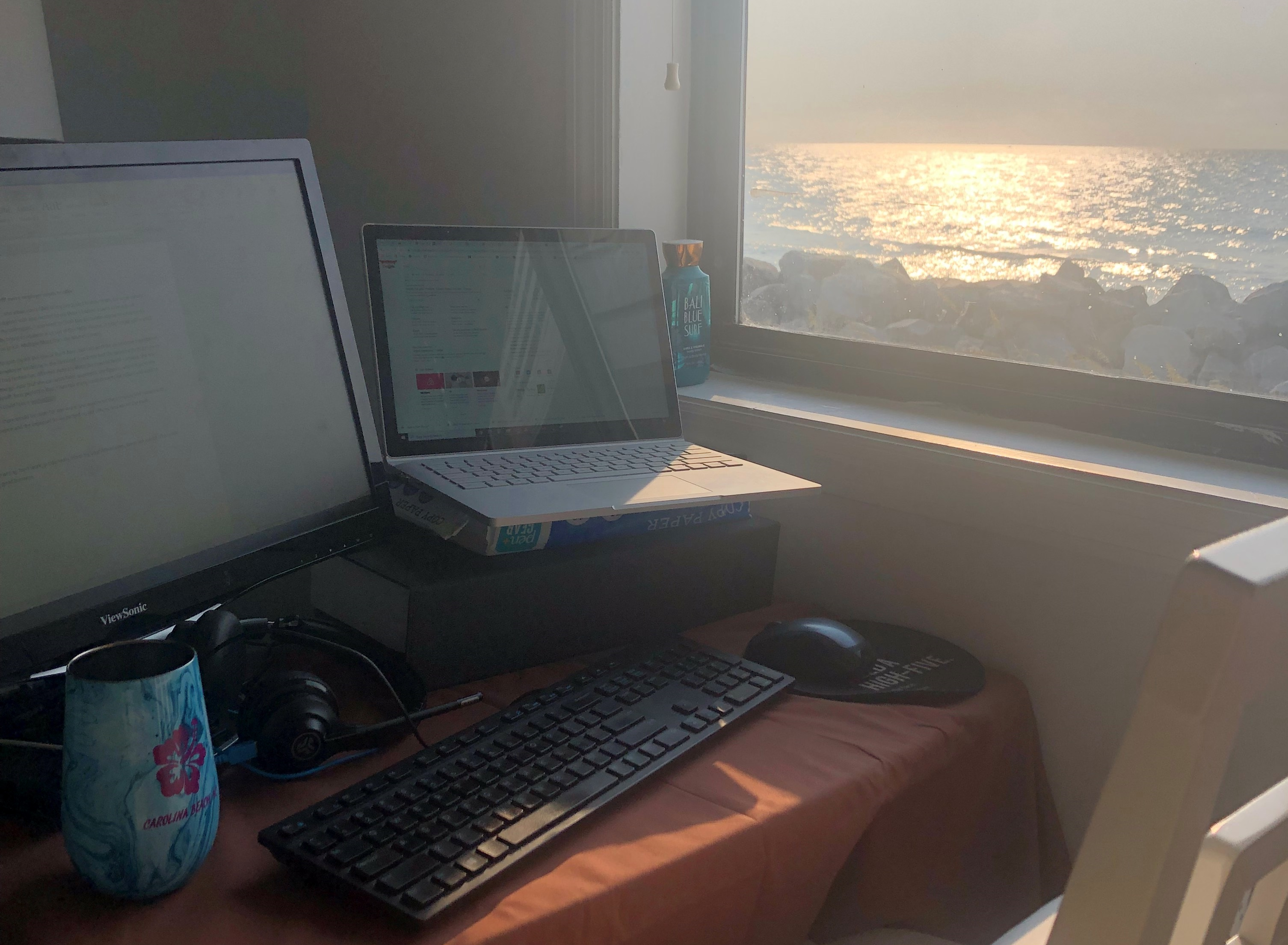 This image shows a computer on a desk with a window that has a view of the ocean.