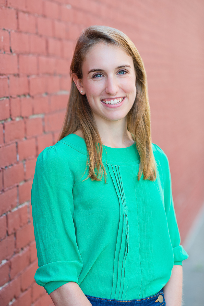 Portrait of Senior Consultant Abigail Rosenson standing outside with a brick wall in the background while wearing light green shirt.