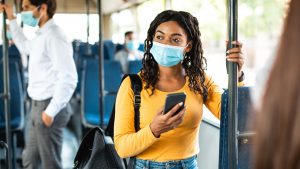 A woman rides transit while wearing a mask.