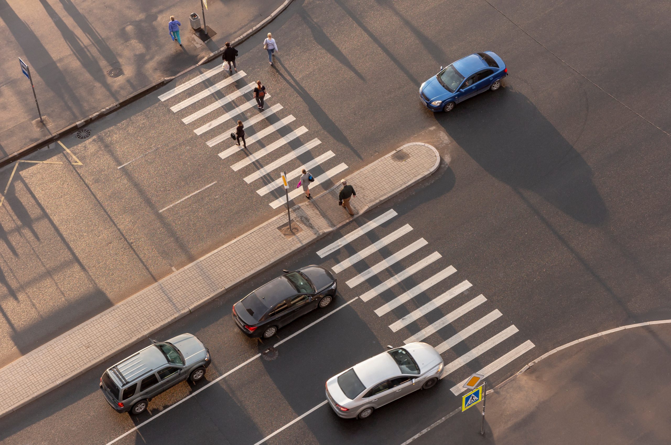 Cars and pedestrians at an intersection with a crosswalk.