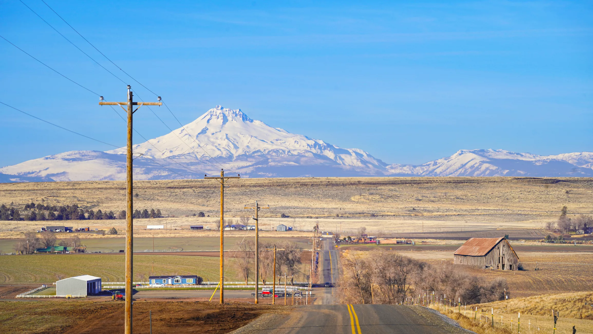 Rural Oregon road with snow-covered mountains in the background, illustrating geographic barriers to transportation access and travel behavior in underserved communities.