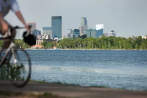 Cyclist riding along the waterfront with the Minneapolis skyline in the background, illustrating multimodal travel in urban areas.
