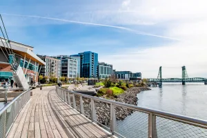 Waterfront path in downtown Vancouver, Washington, with mixed-use buildings along the Columbia River and the Interstate Bridge in the distance.