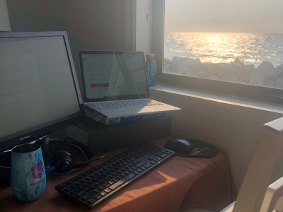 This image shows a computer on a desk with a window that has a view of the ocean.